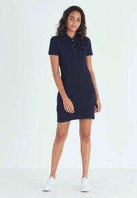 Tummansiniset polo-mekko, joka on muotoiltu istuvaksi, lyhyet hihat, kolme nappia yllä, ja ribattua kaulusta; yhdistetty valkoisiin tennareihin.