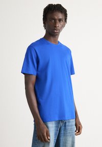 Camiseta de algodón azul con mangas cortas, escote redondo y corte relajado. Destaca por su color sólido y textura suave.