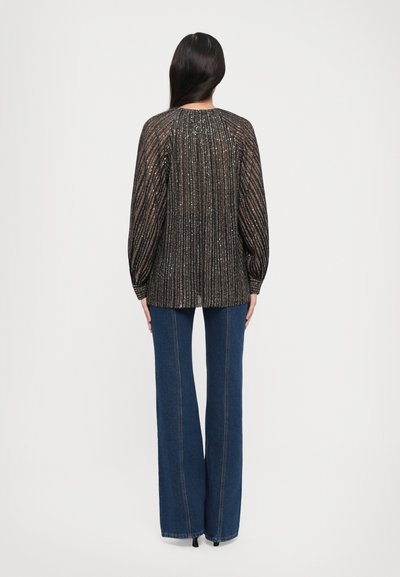 Blusa nera a righe metalliche con maniche lunghe a sbuffo; abbinata a jeans a gamba larga blu scuro a vita alta; texture liscia.
