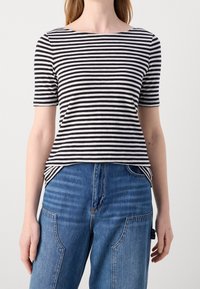 Camiseta de manga corta con rayas blancas y negras y escote barco, combinada con jeans de mezclilla azul de talle alto con detalles únicos en las costuras.
