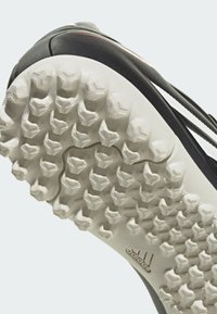 Nahaufnahme der schwarz-weißen Adidas-Schuhsohle mit strukturierten Stollen, die für Grip auf Sportflächen entwickelt wurden.