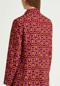 Blusa colorata con motivo a ovali sovrapposti in tonalità di rosa, arancione e rosso, con una texture del tessuto liscia e un design con colletto.