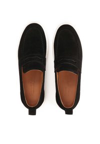 Zapatos en ante negro tipo slip-on con suela blanca, forro de cuero y pequeña lengüeta trasera para facilitar el calce. Diseño minimalista con detalles sutiles de costuras.