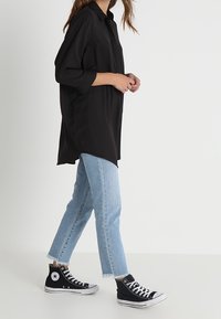 Camicia nera a maniche lunghe con bottoni, jeans dritti blu chiaro con orlo sfilacciato e sneakers nere alte. Tessuto liscio senza motivi.