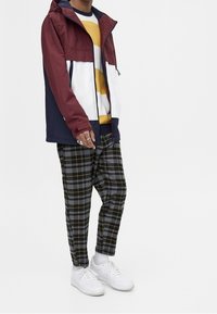 Kleurige jas in bordeauxrood, wit en marineblauw; grijze geruite broek; geel-wit gestreepte trui; witte sneakers; relaxed fit.