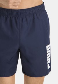 Bañador azul marino hecho de material ligero; cinturilla elástica; presenta un gran logotipo blanco de "PUMA" en el lado izquierdo.