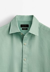 Hellgrünes Hemd aus strukturiertem Stoff mit spitzem Kragen, fünfknöpfiger Knopfleiste und einem Etikett innen im Kragen.