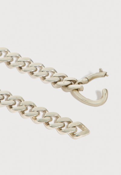 Chaîne argentée épaisse avec un fermoir cassé reposant sur un fond clair.