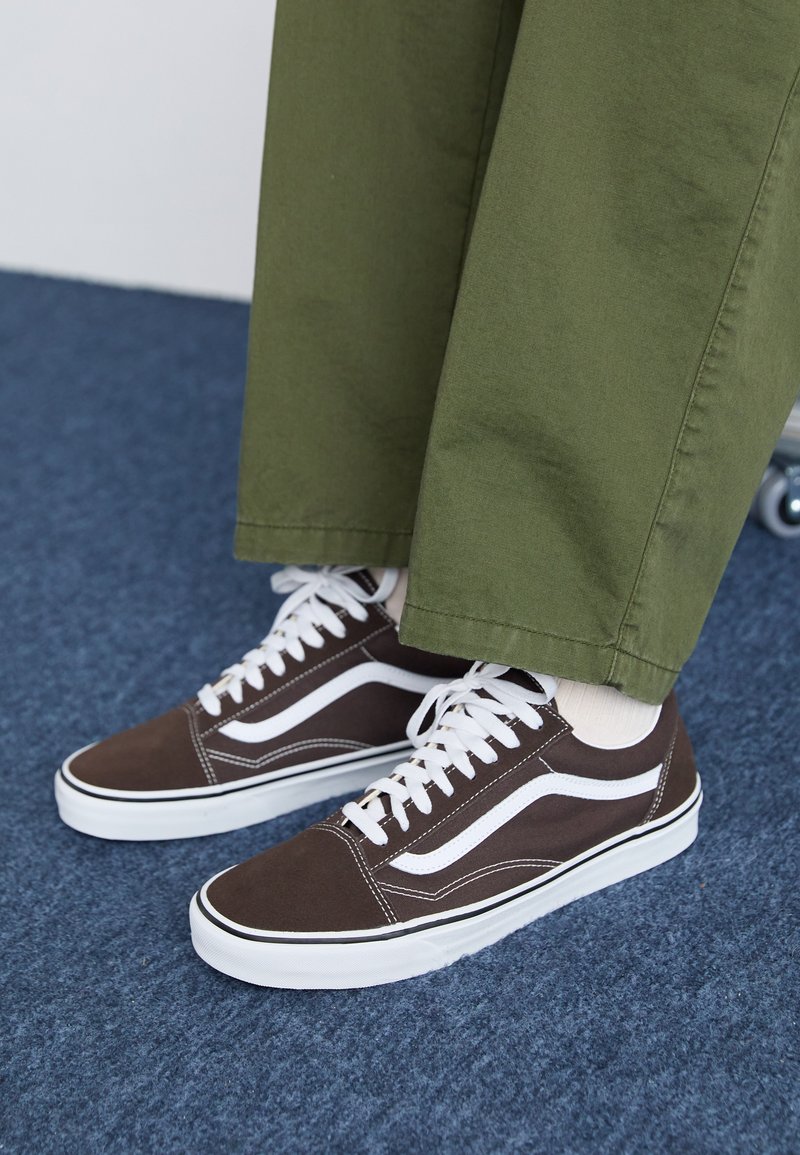 Brune lerretsneakers med hvite detaljer, med et klassisk design, hvite snøringer og en gummisåle, sammen med grønne bukser.