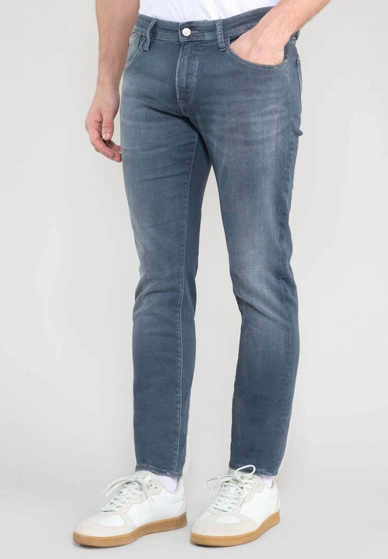 Vaqueros de mezclilla azul claro con un corte ajustado, que cuentan con bolsillos frontales y un cierre de botón, combinados con zapatillas blancas.