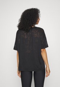 Czarny przezroczysty, oversize t-shirt z krótkimi rękawami, o luźnym kroju i delikatnej fakturze. Noszony z czarnymi legginsami.