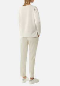 Light beige sweatshirt with a relaxed fit, crew neck, and ribbed cuffs, paired with matching slim-fit pants and white sneakers.