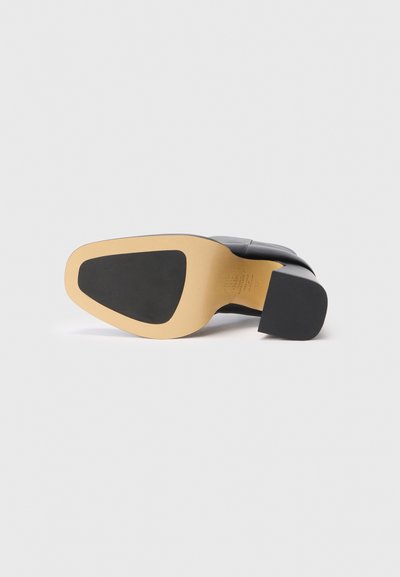 Zapato negro de tacón alto con parte superior de cuero suave y suela de goma beige. La puntera cuadrada y el tacón ancho y de bloque proporcionan estabilidad.