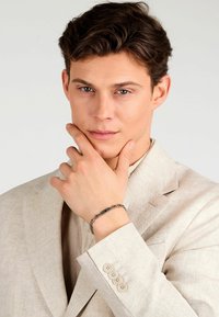 Svetlo bež laneni kostim z enojnim zapenjanjem, dopolnjen s srebrno zapestnico z okroglimi poudarki in pravokotno sponko.