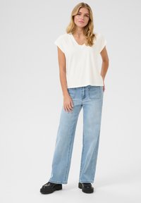 Witte v-hals t-shirt met kapmouwen, gecombineerd met lichtblauwe wijde jeans. Zwarte platform schoenen maken de casual look compleet.