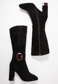 Botas altas de ante negro, con punta afilada, tacón grueso, cremallera lateral y un detalle decorativo de hebilla en la correa del tobillo.