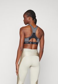 Grå sports-bh med utskjæringsdesign, med et svart Techfit-bånd, kombinert med høyt falte kremfargede tights med teksturerte detaljer.