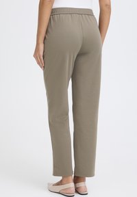 Khakifarbene, elastische Hosen mit geradem Bein, aus weichem Material hergestellt, mit einer glatten Textur und minimalen Nähten.