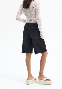 Pantalones cortos de mezclilla negros con dobladillo deshilachado, dos bolsillos traseros, combinados con sandalias de plataforma beige. La parte superior tiene un diseño de encaje blanco texturizado.