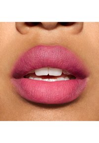 Rouge à lèvres mat d’une teinte rose vif sur des lèvres lisses et pulpeuses avec une finition naturelle et des détails de texture visibles. Les dents blanches sont légèrement visibles.