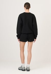 Čierny bavlnený set so sweatshirtom a šortkami, s voľným strihom, dlhými rukávmi a mäkkou textúrou. Skombinovaný so šedými atletickými topánkami a bielymi ponožkami.