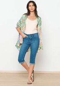 Daudzkrāsains viegls kimono ar viļņu rakstiem, bēšs topiņš, zili džinsa ¾ bikses un metāla sandales, uz neitrāla fona.