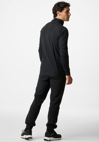 Zwarte sportieve fleece top met een hoge kraag, lange mouwen, ribbeltextuur, gecombineerd met bijpassende zwarte joggers en zwarte sportschoenen.
