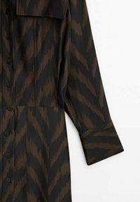 Chemise noire avec motif zigzag marron, manches longues et détails à boutons. Fabriquée dans un matériau doux avec une coupe décontractée.