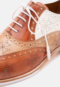 Καφέ και μπεζ δερμάτινο παπούτσι επίσημου τύπου δύο αποχρώσεων με λευκά κορδόνια και διακοσμητικά διάτρητα σχέδια brogue.