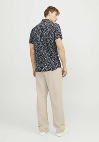 Camicia floreale a maniche corte di colore blu navy con colletto spread, abbinata a pantaloni beige a gamba larga e sneakers bianche, vista dal retro.