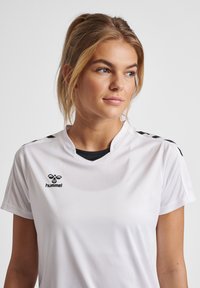 White performance shirt with a black collar and shoulder accents, featuring a logo on the chest and short sleeves. Smooth fabric texture.