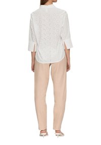White, eyelet top with three-quarter sleeves, back slit detail, paired with loose beige trousers and white heeled sandals.