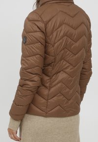 Brun oppustet jakke med zigzag mønster, blank overflade og høj krave. Har et sort logo-patch på ærmet.