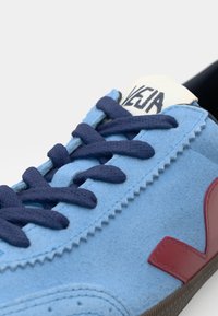 Sníker azul em camurça com atacadores azul-marinho, língua branca e detalhe em logo vermelho. Parte superior texturizada e detalhe em costura contrastante. Sola de borracha.