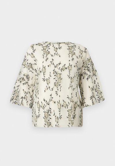 Haut brodé de fleurs en crème, avec des manches courtes et larges et une surface texturée ornée de motifs floraux vert foncé et beige.