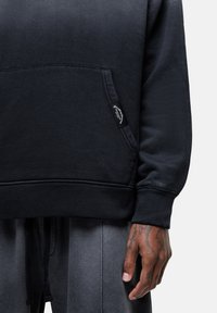 Felpa nera con tasca frontale, polsini e orlo a costine. Presenta un tessuto texturizzato e un'etichetta laterale. Abbina dei pantaloni grigi.