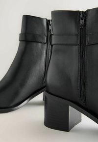 Mustad nahast pahkluu saapad, millel on tõmblukk, ruudukujuline konts ja minimalistik disain. Sile tekstuur koos kontrastsete õmblusdetailidega.