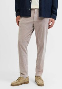 Lys beige kordfløjl bukser med lodrette ribber, afslappet pasform og sidelommer, parret med brune ruskinds sko og en mørk denim skjorte.