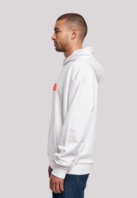White hoodie made from soft fabric, featuring a kangaroo pocket, a drawstring hood, and red text on the chest. Casual fit and blue denim jeans.