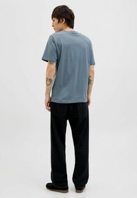 Blå kortærmet T-shirt i blødt bomuld, parret med sorte vidde bukser. Outfittet har synlige tatoveringer på armene.