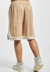 Shorts de basket rayés beige avec une texture en maille, présentant une bordure blanche et dorée au niveau de l'ourlet, une taille élastique et une coupe décontractée.