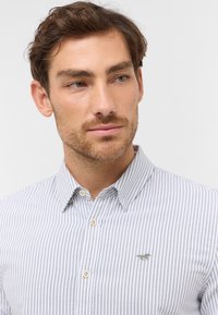 Koszula w paski, button-down, w jasnoniebieskim i białym kolorze, z klasycznym kołnierzykiem, z haftowanym logo na piersi oraz lekką teksturą.