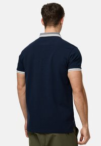 Mørkeblå polo t-shirt i bomuldsmateriale, med en kontrasterende stribet krave og manchetter, korte ærmer og en lige søm ved taljen.