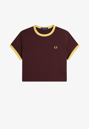 Camiseta corta de color marrón oscuro con cuello y puños amarillos, que presenta un pequeño logo de corona de laurel amarilla en el pecho izquierdo.