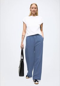 Fehér rövid ujjú felső és laza, kék, széles szárú nadrág elasztikus derékpánttal. Fekete kézitáska és fekete sportcipő bézs színű részletekkel.