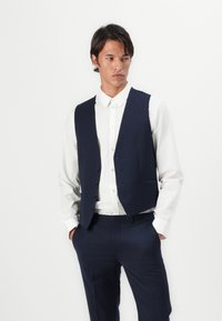 Marineblaue Weste mit einem eleganten Design, fünf Knöpfen und zwei Taschen, getragen über einem weißen Hemd, was ein gepflegtes, maßgeschneidertes Erscheinungsbild erzeugt.