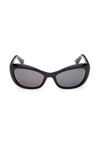 Lunettes de soleil noires surdimensionnées en forme d'œil de chat avec des verres teintés foncés et une finition brillante, nom de la marque « Guess » gravé sur le coin supérieur droit du verre.