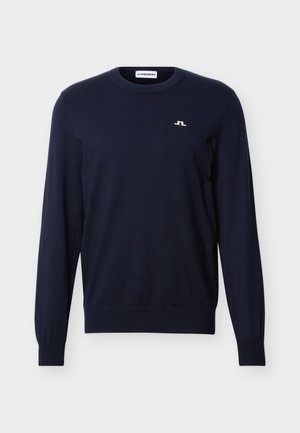 Temno modra majica z dolgimi rokavi in okroglim izrezom, z majhnim belim logotipom na levi prsni strani ter rebrastimi manšetami in spodnjim robom.