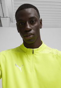 Puma zip-up shirt in felgeel, met een textuurpatroon, korte kraag en een wit logo op de borst. Lichtgewicht stof.