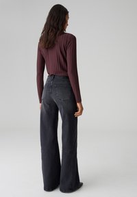 Haut long à manches longues côtelé bordeaux associé à un jean en denim sombre à taille haute et jambes larges, avec des poches arrière et une texture lisse.